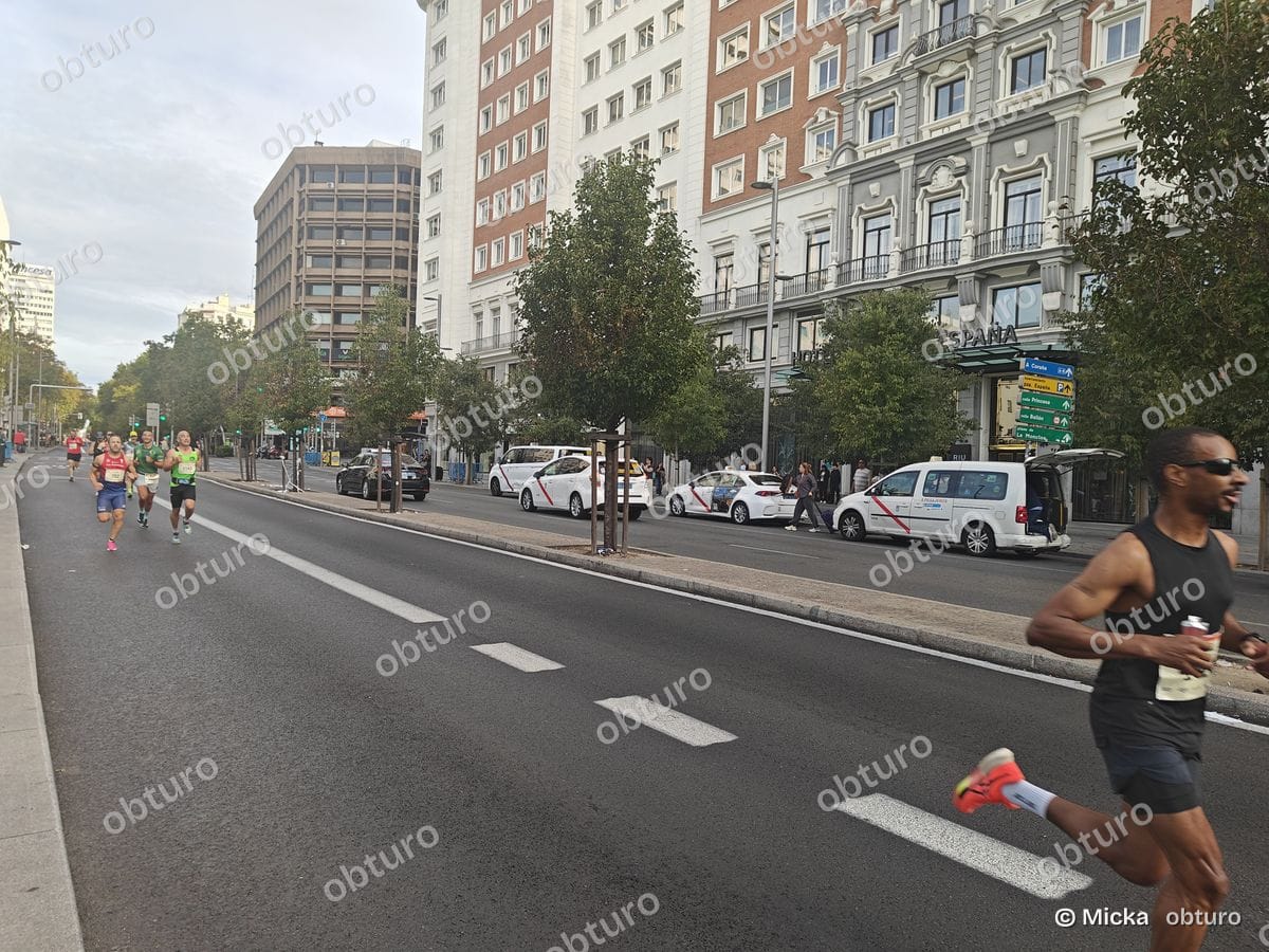 Plusieurs participants courent sur une route urbaine lors d'une compétition sous un ciel légèrement nuageux.