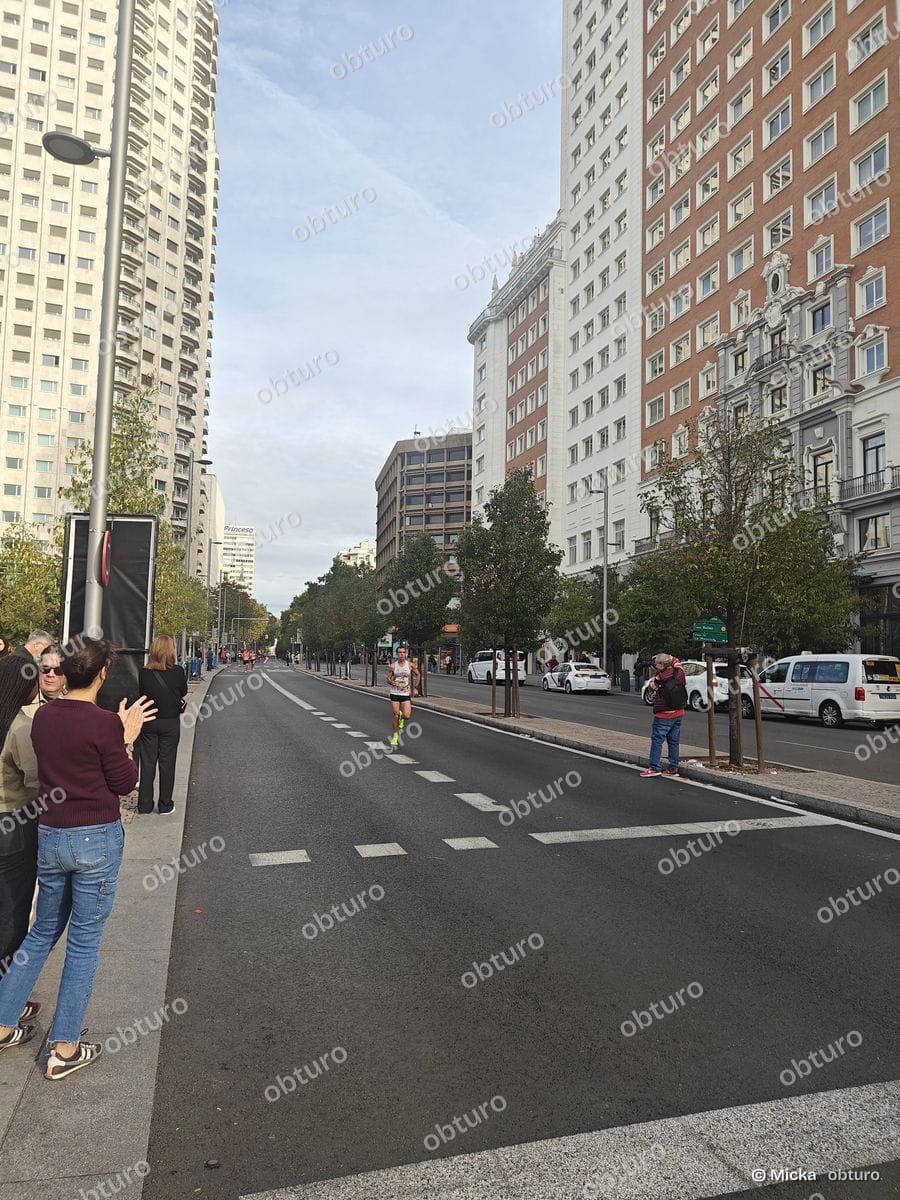 Un coureur participe à une compétition urbaine en traversant une avenue bordée de bâtiments sous un ciel légèrement nuageux.