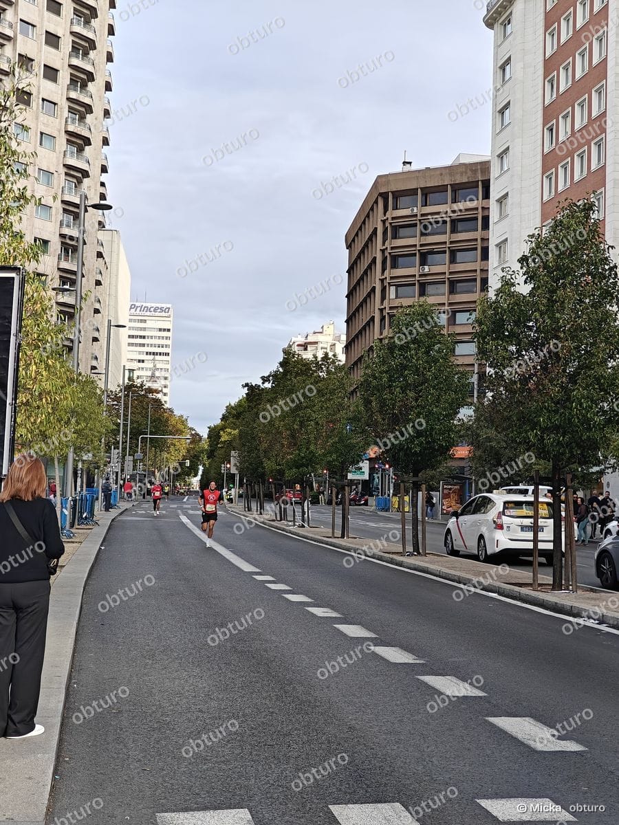 Un marathon urbain se déroule sur une avenue bordée d'immeubles, avec des participants au départ sous un ciel légèrement nuageux.