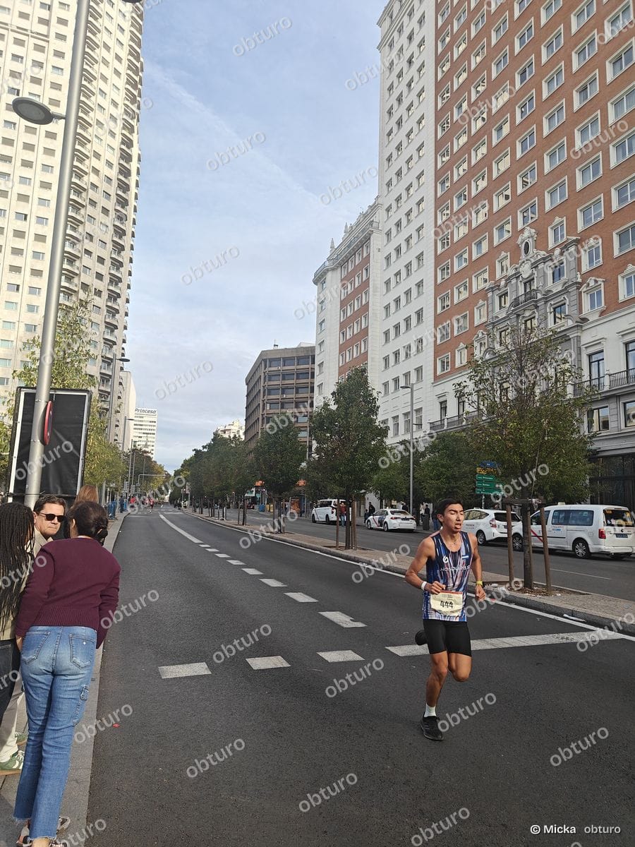 Un coureur traverse une avenue urbaine lors d'une compétition sous un ciel légèrement nuageux.