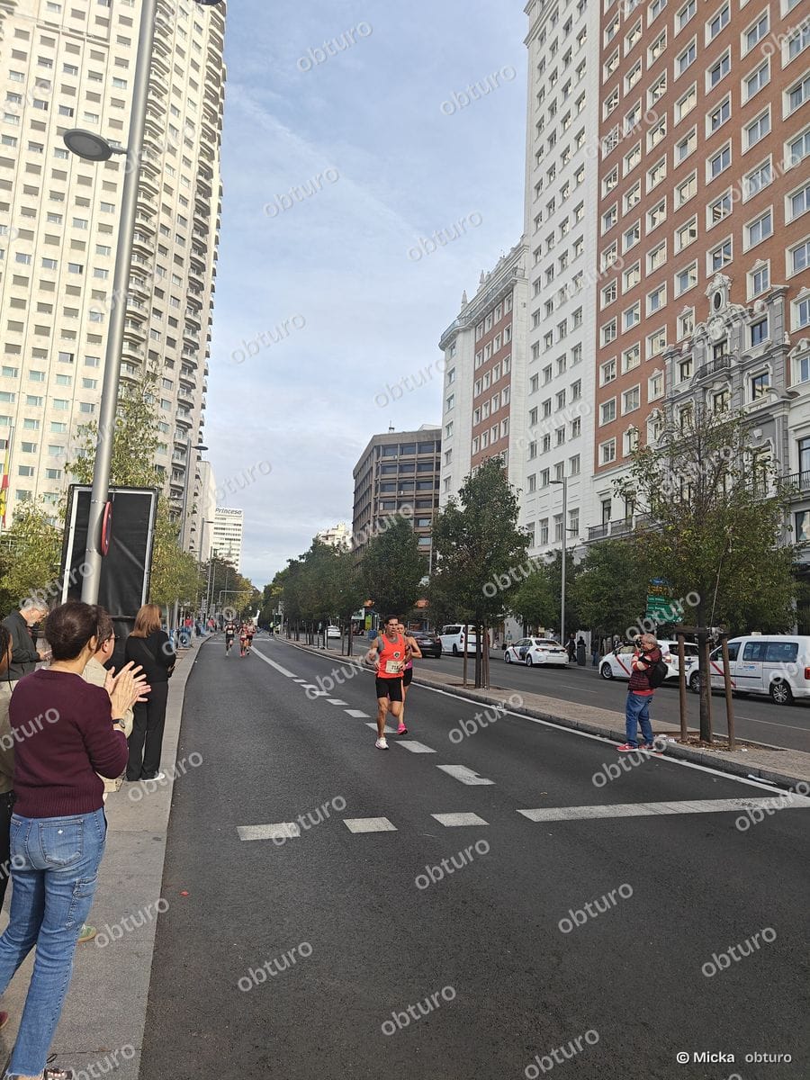 Un marathon urbain se déroule sur une large avenue bordée de bâtiments, avec des participants en pleine course et un public encourageant.