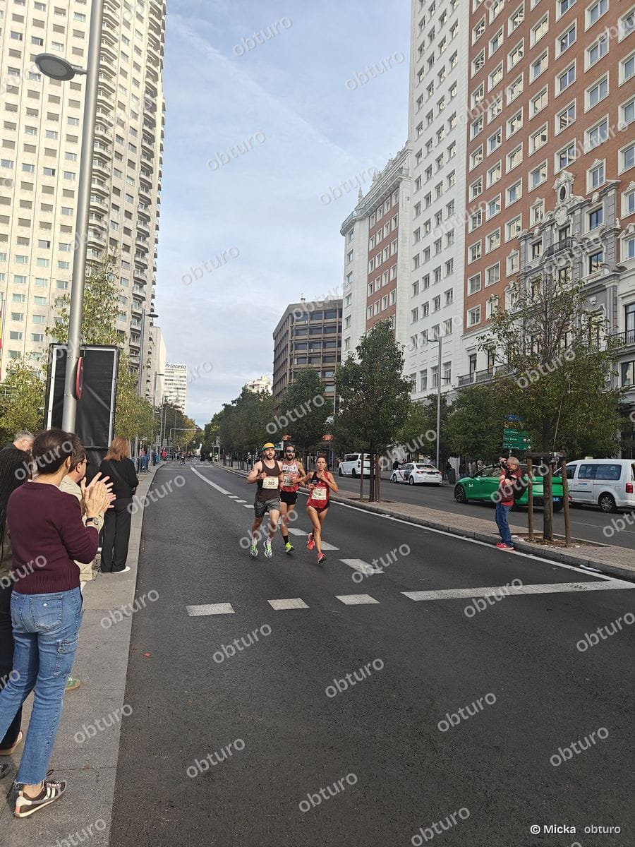 Deux participants courent sur une route urbaine encadrés par des spectateurs sous un ciel légèrement nuageux.